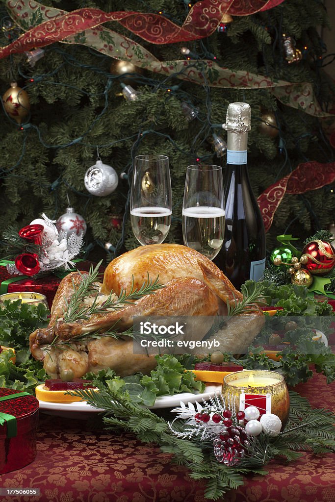 Roasted Christmas Turkey "Christmas-decorated table with feast, gifts, roasted turkey, candles, champagne, and Christmas tree on back." Celebration Event Stock Photo