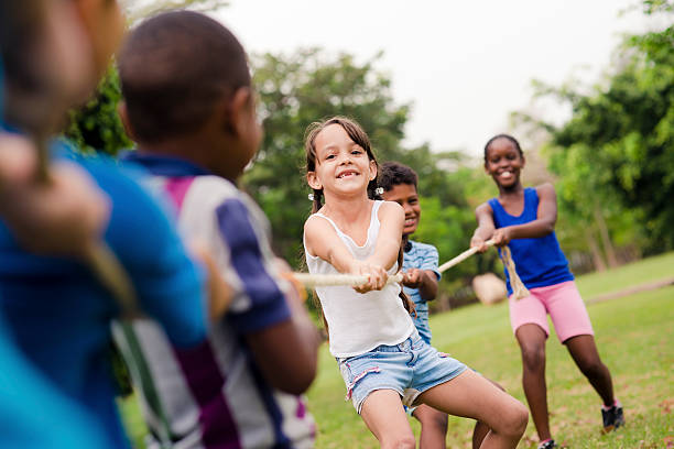 school children playing tug de guerra con cuerda en park - campamento de verano fotografías e imágenes de stock