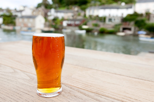 A full pint of English real ale on a wooden table outside a riverside pub.  Differential focus on the glass.