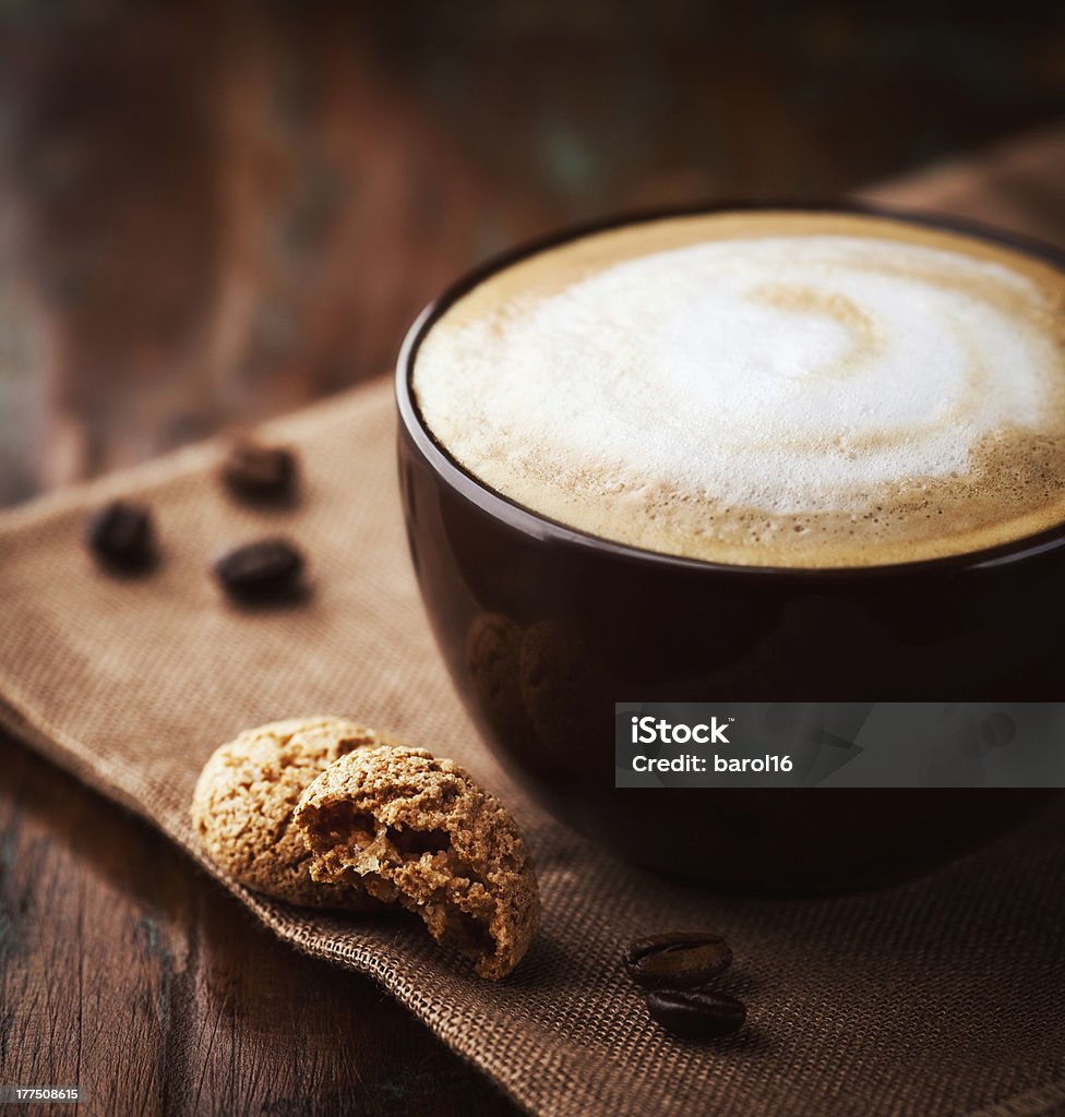 A cup of latte filled to the brim with white and brown foam  cup of latte coffee with biscotti Biscotti Stock Photo