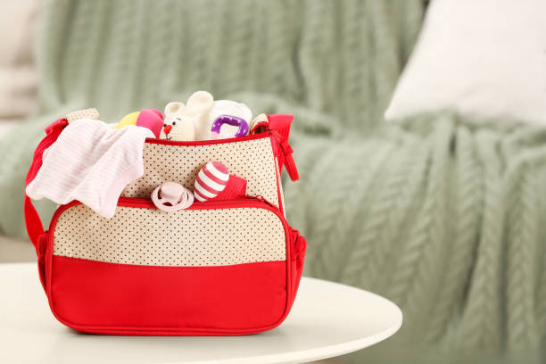 Mother's bag with baby's stuff on white table indoors. Space for text