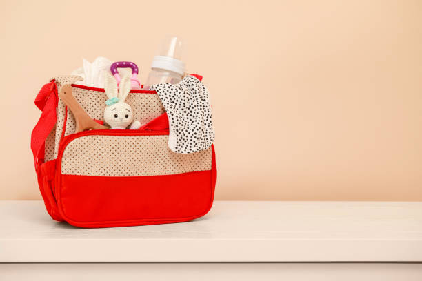 istock Mother's bag with baby's stuff on white table near beige wall. Space for text 1775100552