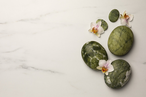 Flat lay composition with spa stones and orchid flowers on white marble table. Space for text