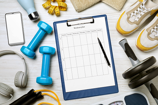 Clipboard with workout plan, smartphone and sports equipment on white wooden table, flat lay. Personal training