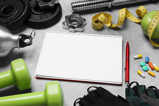 Notebook, apple and sports equipment on grey textured table. Personal training