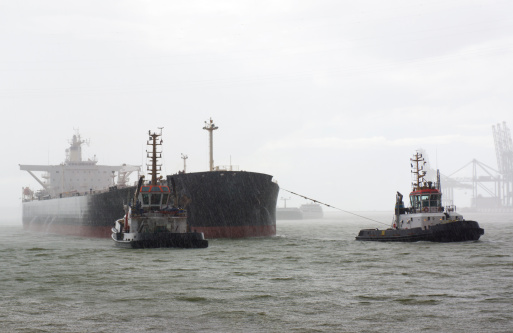 Seagoing cargo vessel and tugboats in heavy rain in the Port of Antwerp