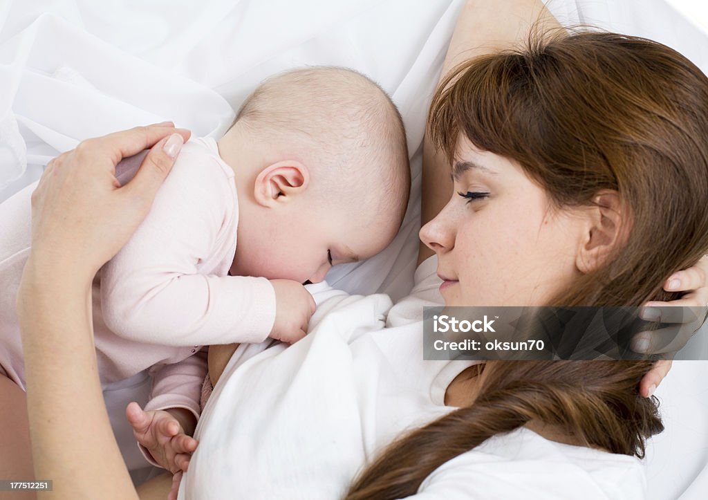 A mother breast-feeding her baby in bed young mother breast feeding her baby girl Breastfeeding Stock Photo