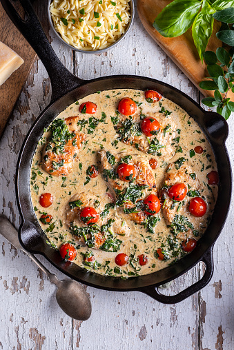 Creamy Tuscan Chicken in a Cast Iron Skillet with Parmesan Cheese, Orzo, Tomato, Basil, Spinach and Oregano