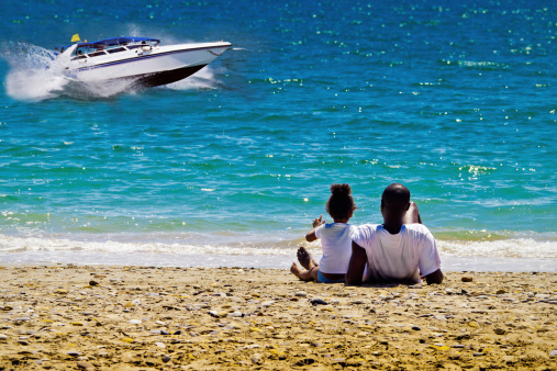 father and daughter sit on the beach and look on Speedboat