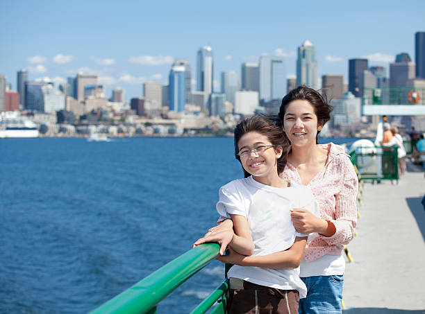 Two sisters on ferry deck with Seattle skyline in background Two sisters on windy ferry deck with Seattle skyline in background ferry deck girls stock pictures, royalty-free photos & images