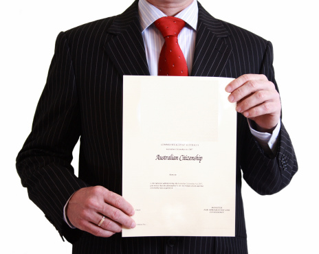 Man in black suit holding Australian Citizenship Certificate on isolated white background