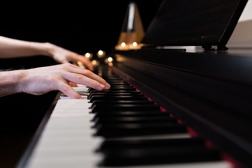 Hands playing the piano keyboard closeup and candle light bokeh background. Male pianist learning to play the piano instrument and beautiful music. Reading sheet music with metronome.