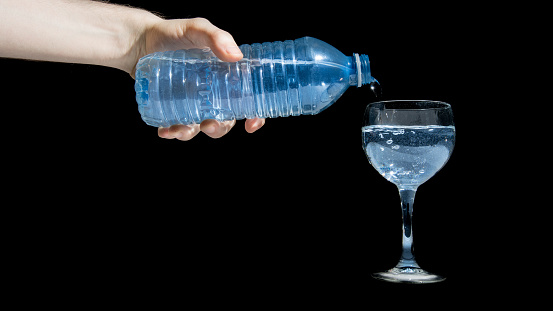 Pouring a glass of water from water bottle refreshing drink isolated black background. Filling glass with sparkling blue water.