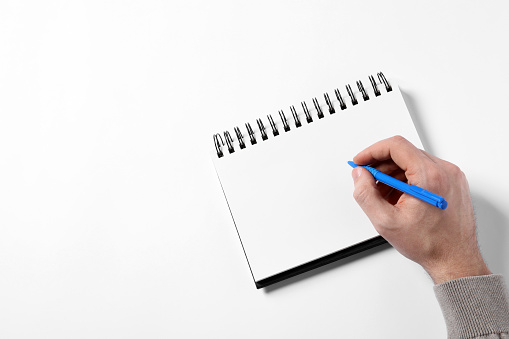 Man with pen and empty notepad on white background, top view. Space for text