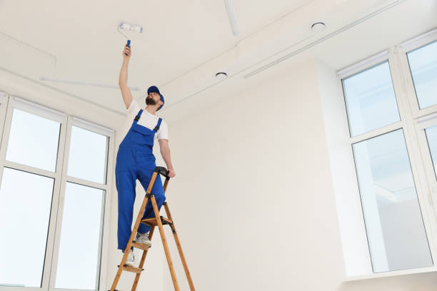 istock Worker in uniform painting ceiling with roller on stepladder indoors, low angle view 1775145271