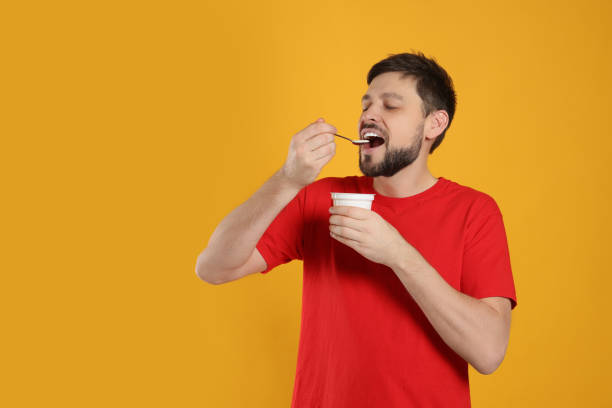 istock Handsome man eating tasty yogurt on orange background 1775145281