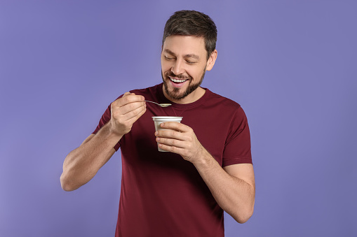 Handsome man with tasty yogurt on purple background