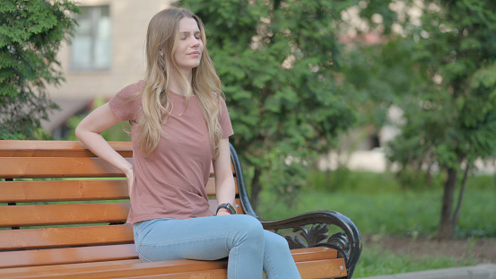 Young Woman with Back Pain Sitting Outdoor on a Bench