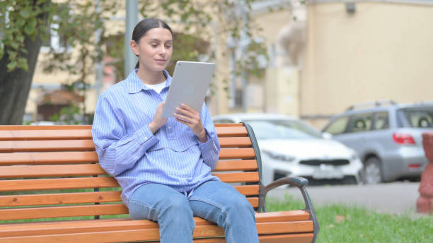 mujer latina usando tableta mientras está sentada al aire libre en un banco - 15838 fotografías e imágenes de stock