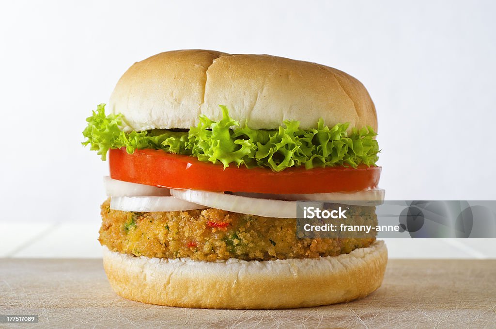 Veggie Burger in Bap A cheese-free vegetarian burger made from vegetables and breadcrumbs, stacked with onion rings, slice of tomato and curly lettuce, in a bap on a wooden board. Veggie Burger Stock Photo