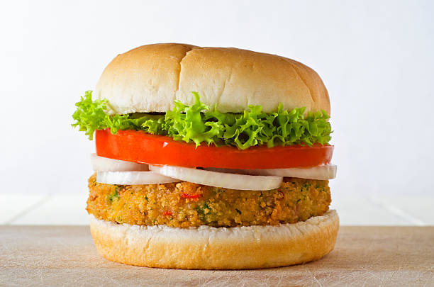 Veggie Burger in Bap A cheese-free vegetarian burger made from vegetables and breadcrumbs, stacked with onion rings, slice of tomato and curly lettuce, in a bap on a wooden board. veggie burger photos stock pictures, royalty-free photos & images