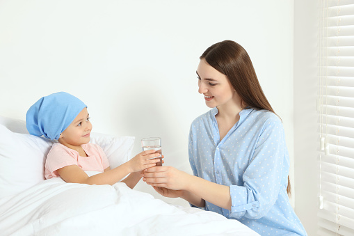Childhood cancer. Mother giving daughter glass of water in hospital