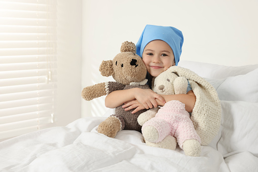 Childhood cancer. Girl hugging toy bunny and bear in hospital