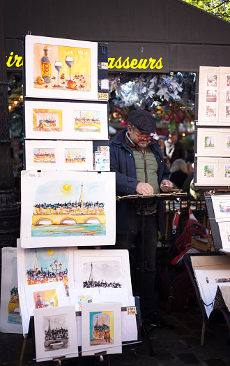 Paris, France: A Montmartre artist at work on the Place du Tertre in the 18th arrondissement, surrounded by his colorful paintings and drawings.