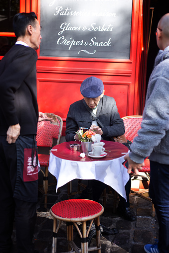 Paris, France: A tourist and waiter outside a red sidewalk cafe on Place du Tertre in the heart of Montmartre; the tourist is looking at his phone.