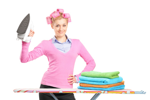A smiling woman with hair rollers holding an iron and ironing board isolated on white background