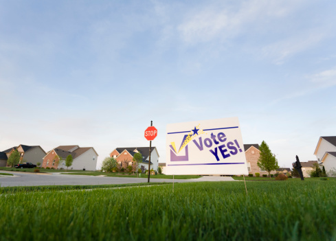 Image of a lawn sign in a neighborhood reading Vote Yes