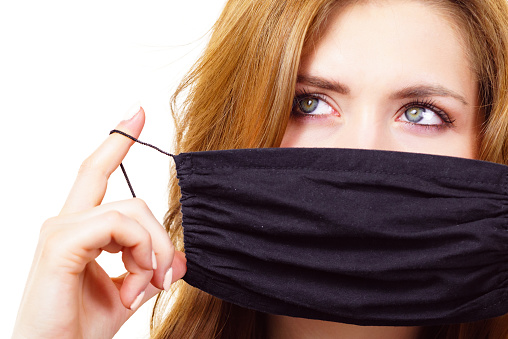 Woman using black protective reusable face mask, covering mouth. Coronavirus prevention. Health and safety.