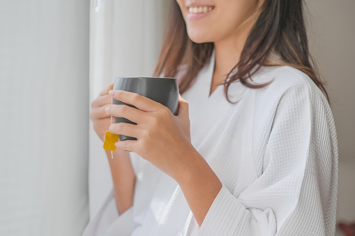 Close-up shot of smiling single female traveller drinking hot tea in hotel room