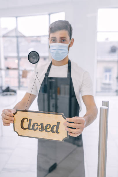 istock Closed, a waiter wearing a protective face mask turns a signboar 1775286680