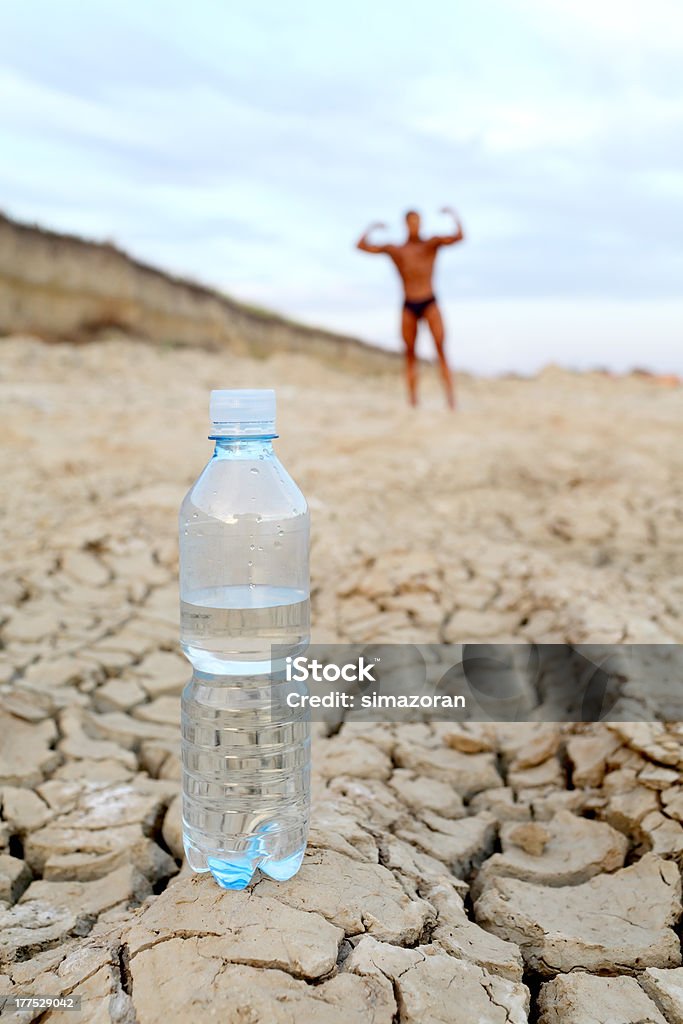 Water Bottle with water at cracked land with man exercising in background Active Lifestyle Stock Photo