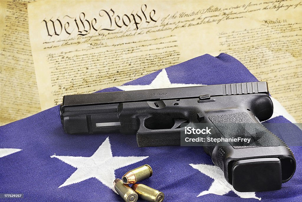 Handgun and Constitution A 45 caliber handgun and ammunition resting on a folded flag against the United States constitution. American Flag Stock Photo