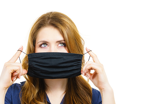 Woman using black protective reusable face mask, covering mouth. Coronavirus prevention. Health and safety.