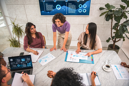 A casually elegant businesswoman with short, curly hair brings vibrancy to a modern office as she presents a compelling data analysis showcased on a digital board.