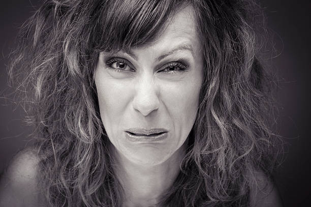 Close-up head shot of woman pulling funny face Close-up of a young woman with sour grimace black and white sour face stock pictures, royalty-free photos & images
