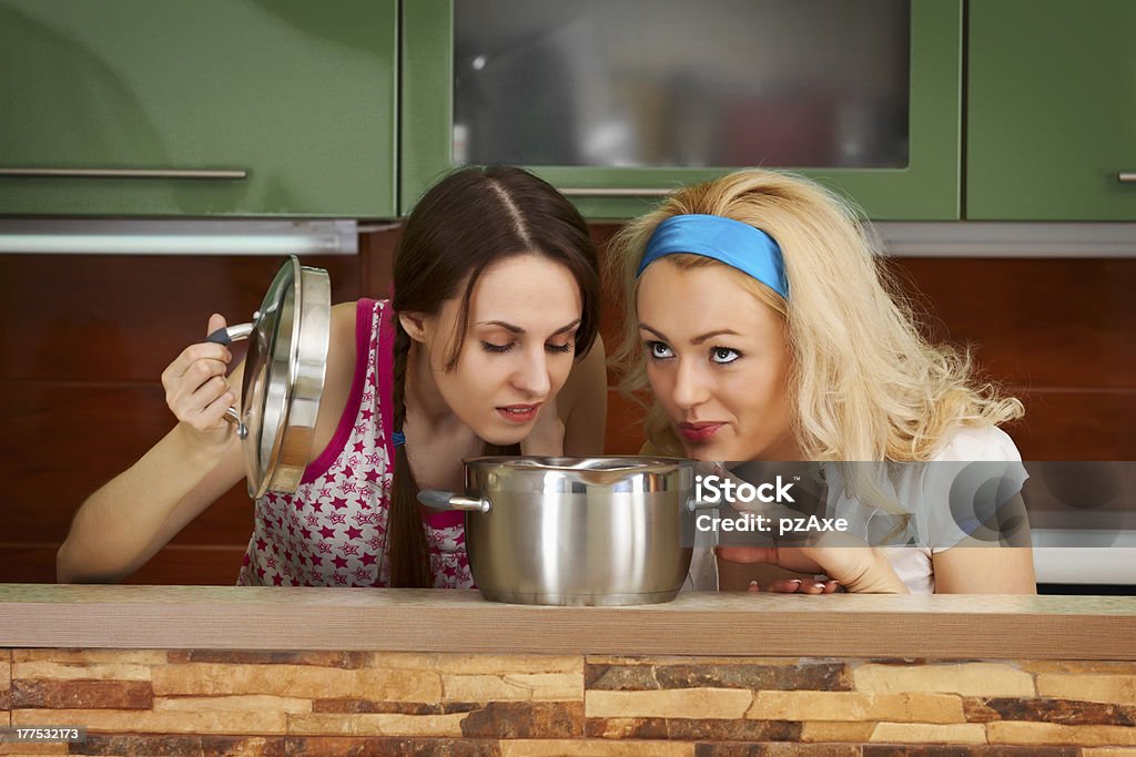 Two young women with a pot of soup Two young women in the kitchen with a pot of soup Bizarre Stock Photo