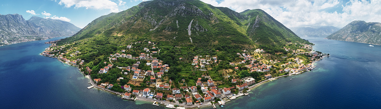 Old houses with red roofs on the seashore on the slope of a green mountain. Montenegro. Drone. Panorama. High quality photo