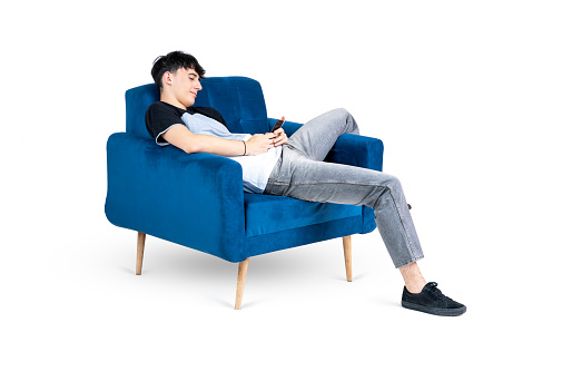 Teenager lying on an armchair, texting, isolated on white background.