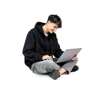 Smiling teenager using a laptop sitting on the floor isolated on white background
