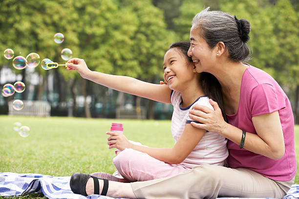 abuela con china granddaughter soplando burbujas en el parque - bubble wand bubble child playful fotografías e imágenes de stock