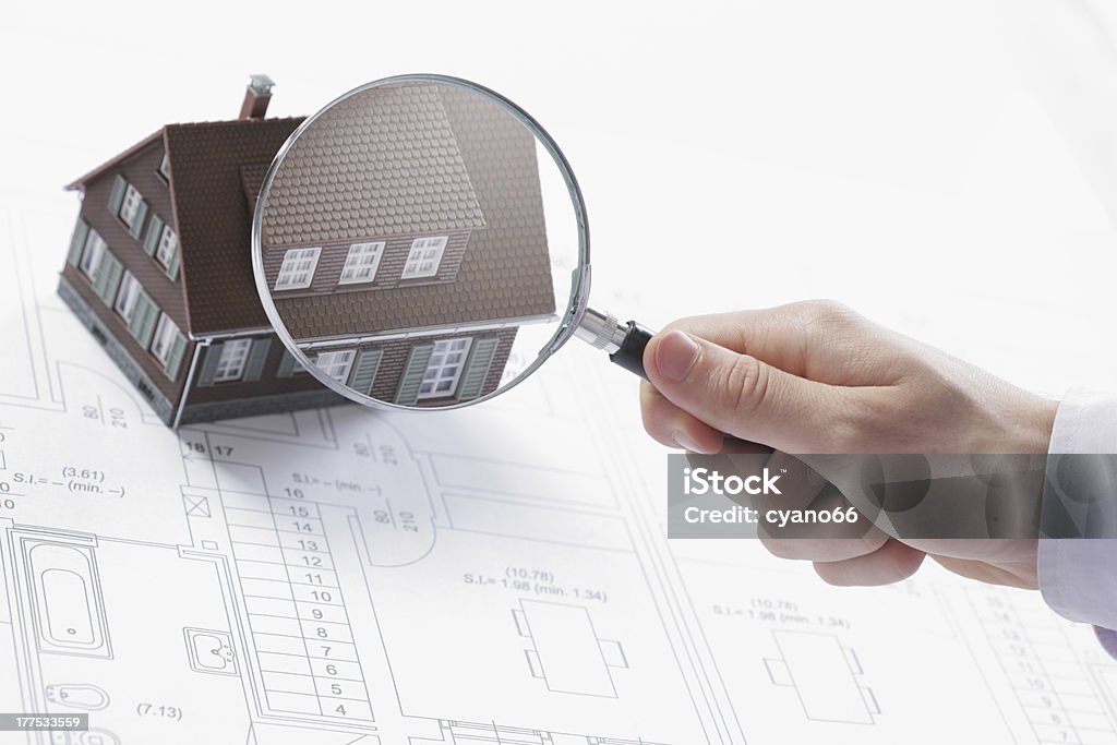 Magnifying glass and house. Concept image of a home inspection. A male hand holds a magnifying glass over a miniature house. Construction Industry Stock Photo