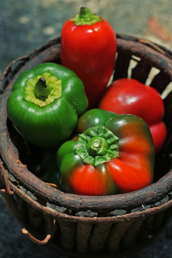 A few small bell peppers in a wood basket.