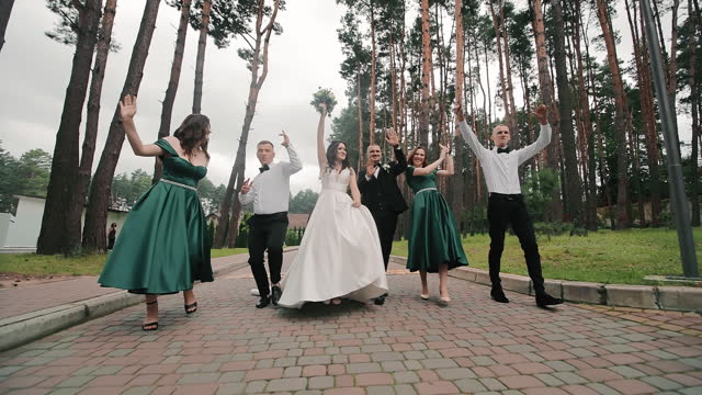 The newlyweds walk in the park together with their bridesmaids and friends of the groom. The newlyweds are walking in the park in a cheerful company of friends