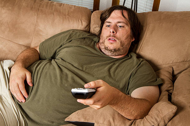 Overweight man watching TV on the couch stock photo