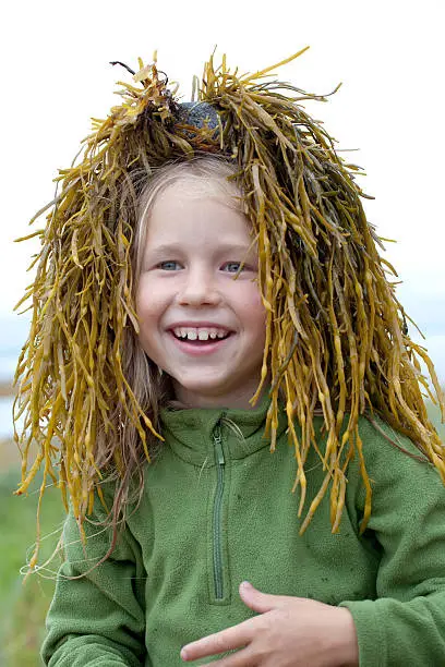 portrait of funny little girl with a wig from green seaweed on her head