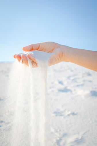 White sand spills around and through female hand.